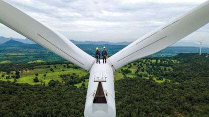 Two men wearing PPE while standing atop a wind turbine
