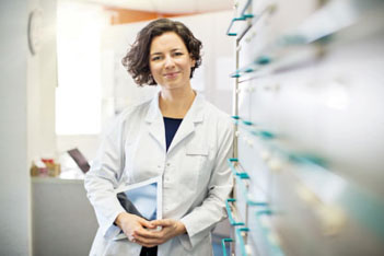 Woman in labcoat leaning against container shelves