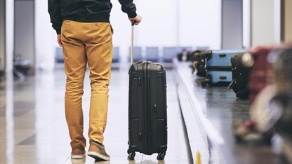 Man in mustard yellow slacks standing with a suitcase at a luggage carousel