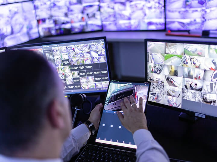 Mature adult man looking at many monitors in front of him using a control panel on a tablet, working in surveillance and security